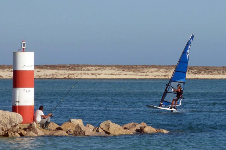 A photo of a surfer going past the entrance to the quay in Fuseta