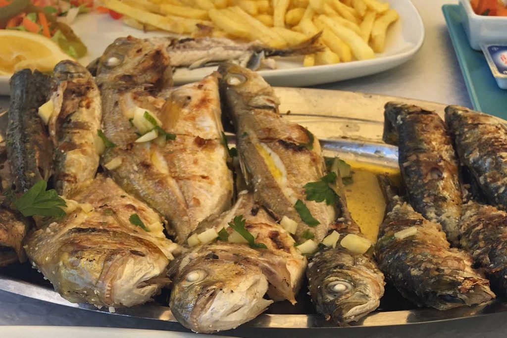 A photo of a plate of grilled fish with chips in the background