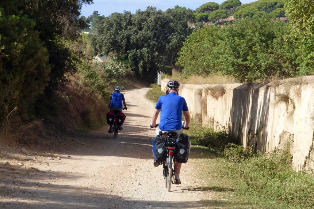 Two cyclists cycling along a dusty track in the Ria Formosa
