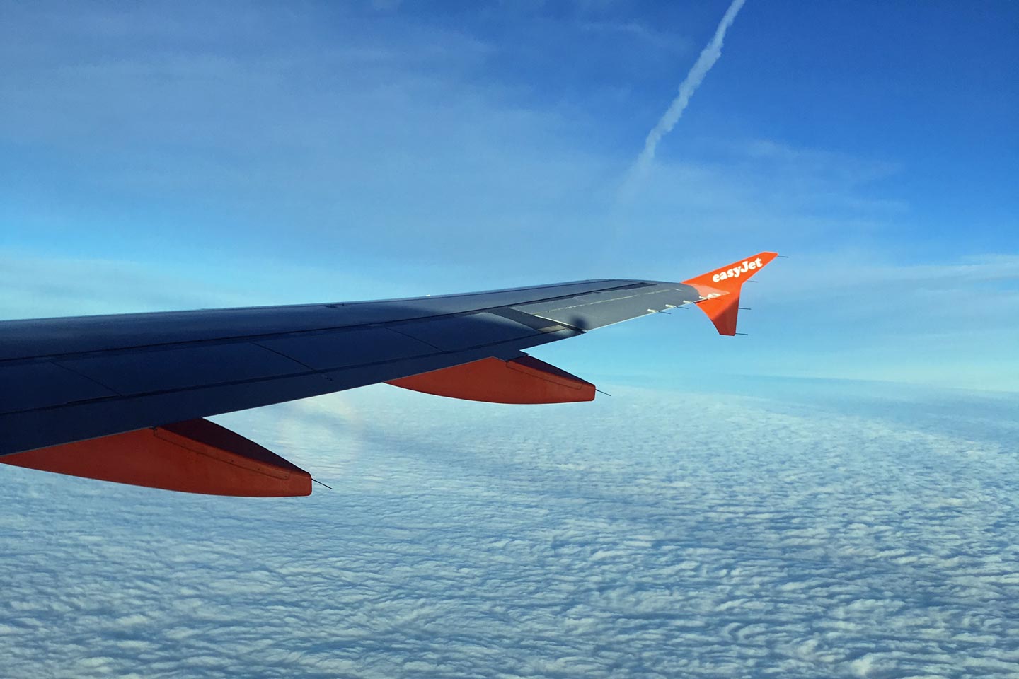 A Photo out of the plane, seing the wing, blue sky and clouds