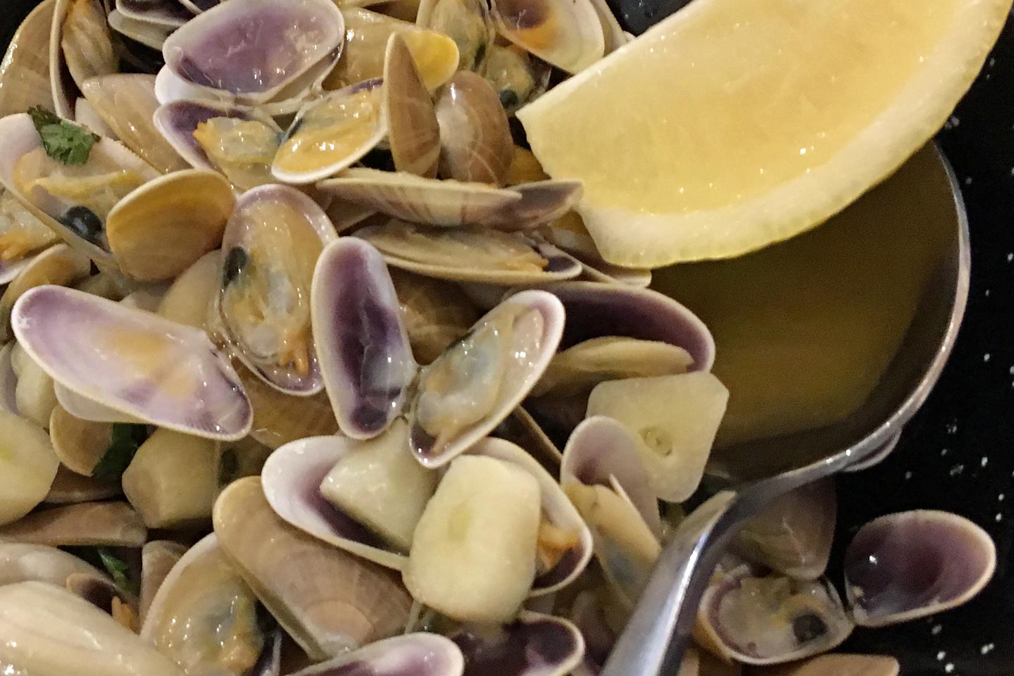 A photo of a plate full of clams with a slice of lemon