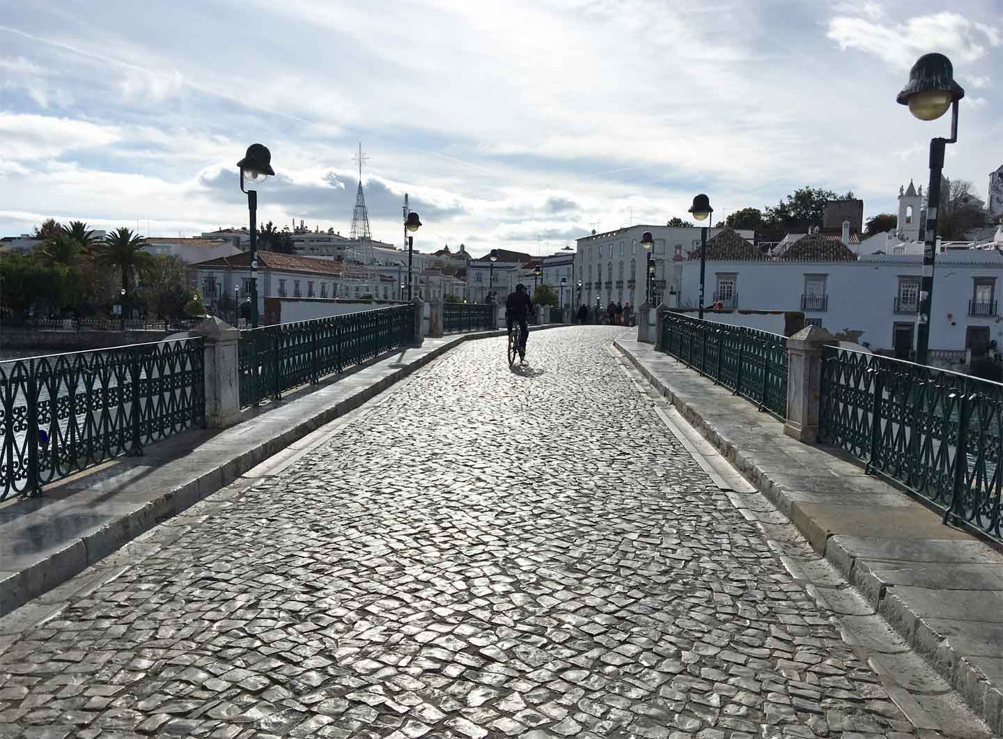 A photo of a cyclist crossing the Ponte Romana in Tavira in the late afternoon